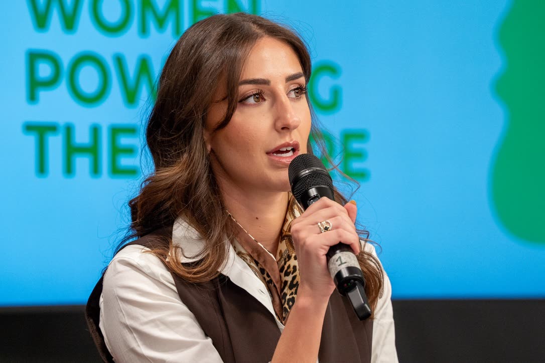 Close-up of Camilla Brossa speaking into the microphone at Women Powering the Future, in a white shirt, brown waistcoat and leopard-print scarf
