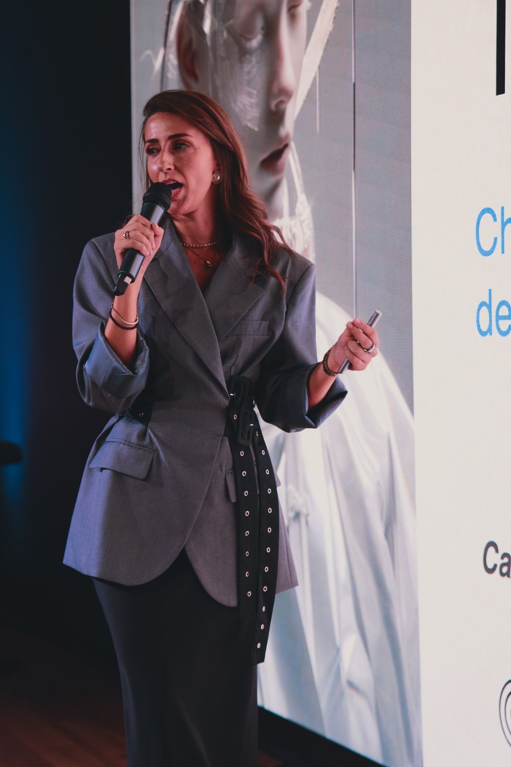 Camilla Brossa speaks into the microphone in front of a slide, holding the presentation clicker