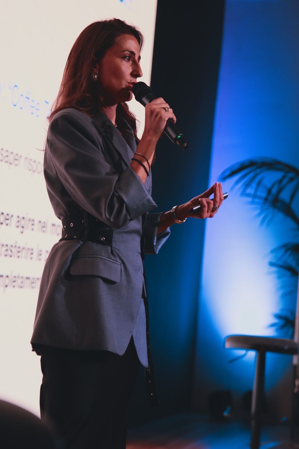 Camilla Brossa in profile at the microphone, in blue light, beside the slides of her talk